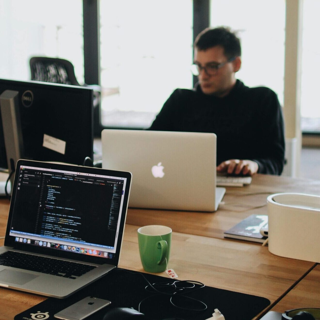 A web developer working on code in a modern office setting with multiple devices.
